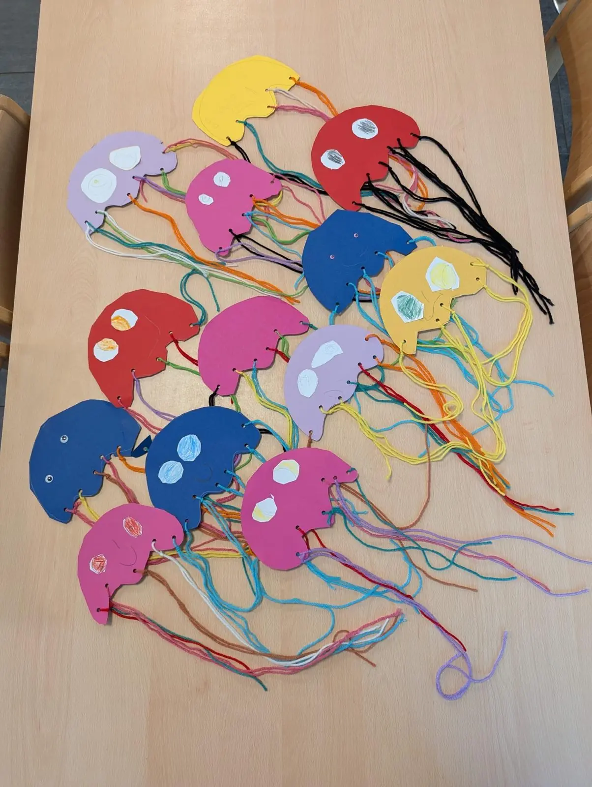 Bunte, von Kindern gebastelte Papierquallen mit Wollfäden auf einem Tisch