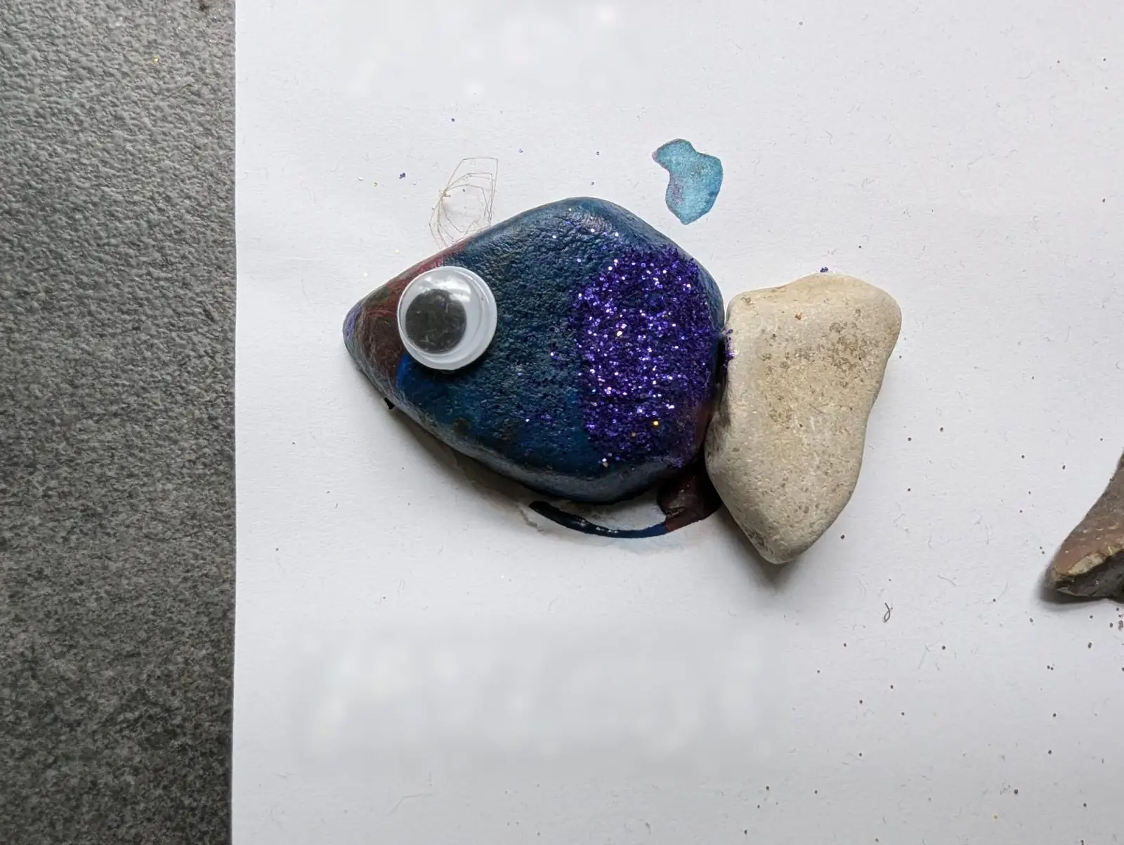Fisch aus einem bemalten Stein mit Glitzer, Wackelauge und Steinflosse